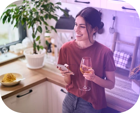 Mulher na cozinha usando o celular enquanto controla a casa inteligente com a Olli